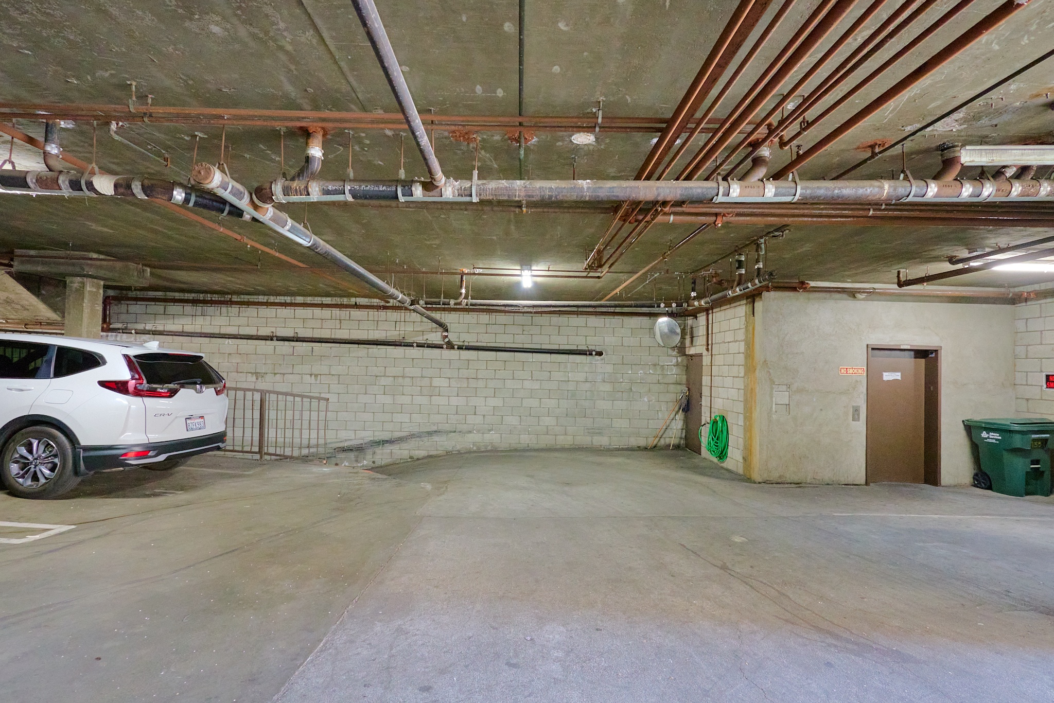 A car is parked in a garage with a wall of pipes running along the ceiling.